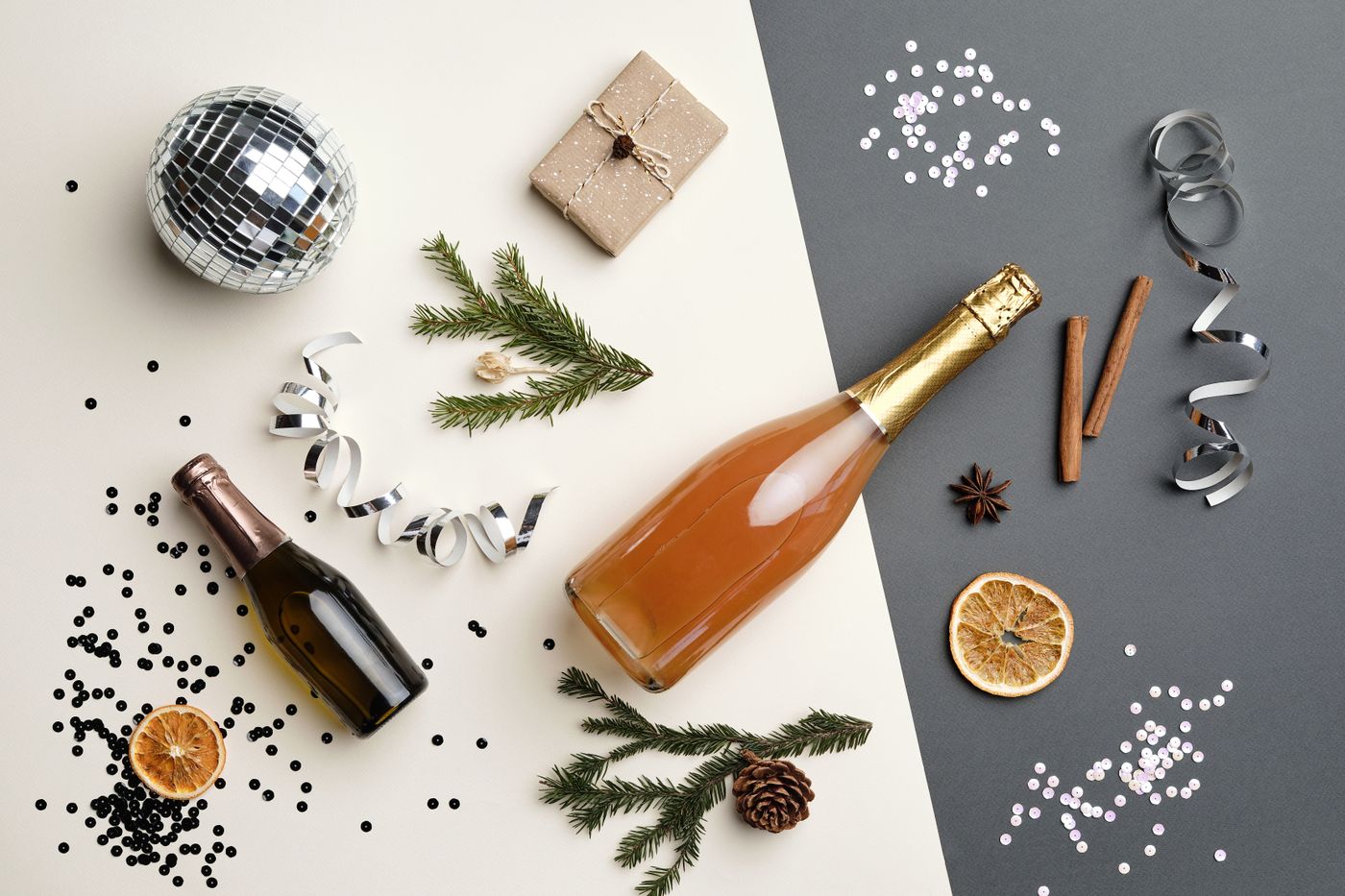 A festive gift-wrapped bottle of sparkling wine beside two glasses, pine branches, and Christmas ornaments on a wooden table