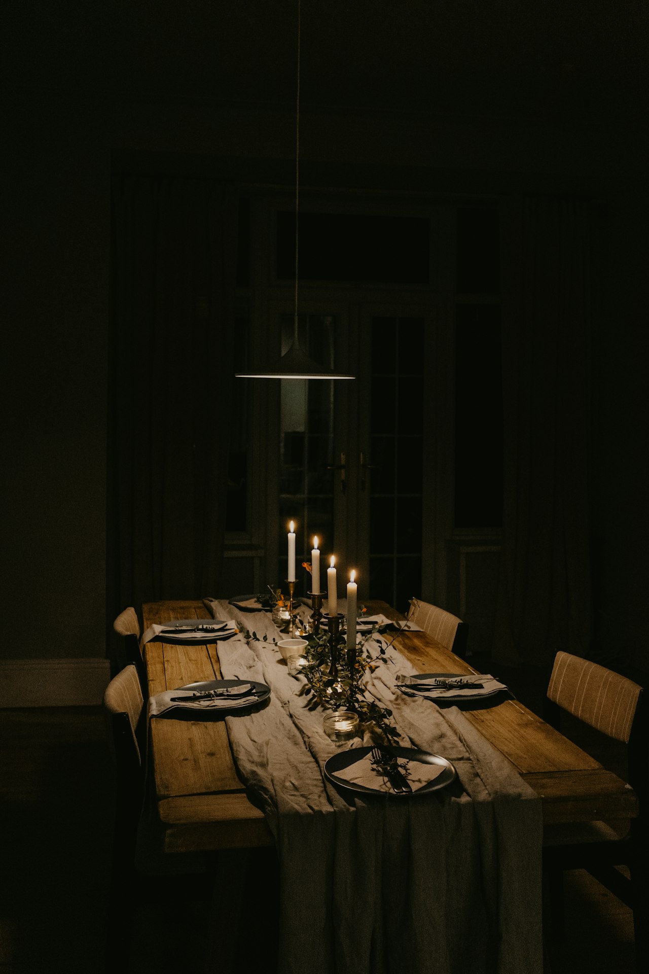 Romantic at-home date night dinner table set with candles, a poured glass of red wine, and pasta