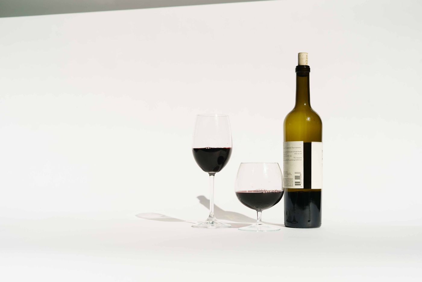 A standard 750 ml bottle of wine beside two poured five-ounce glasses, the start of the five servings it holds