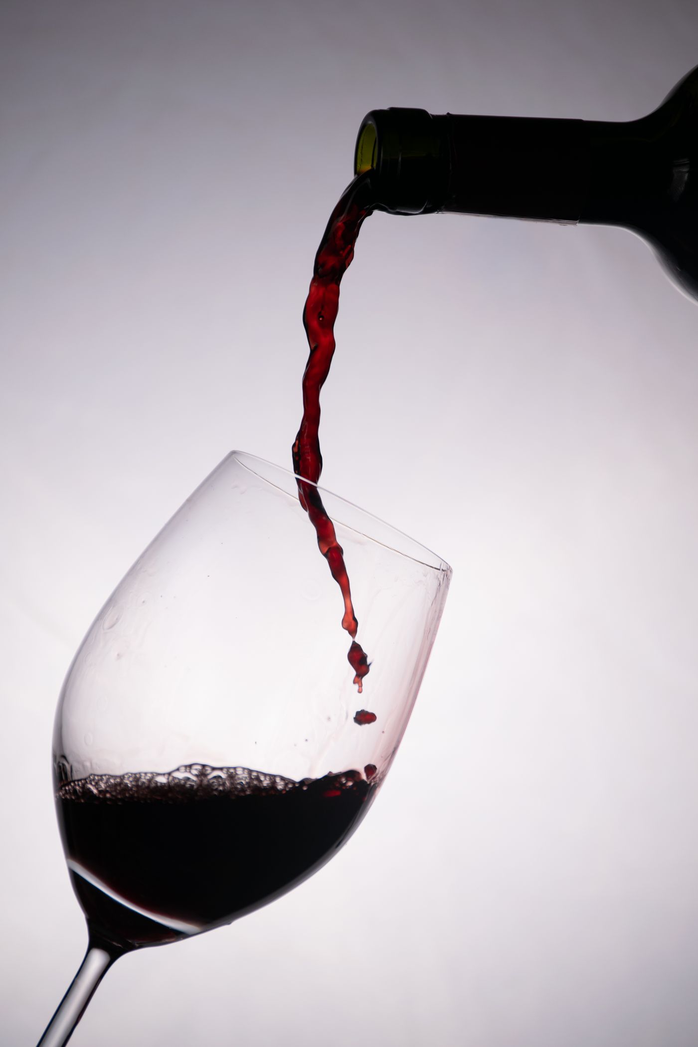 Full bodied red wine being poured into a large glass beside a lighter red, showing the difference in color and weight