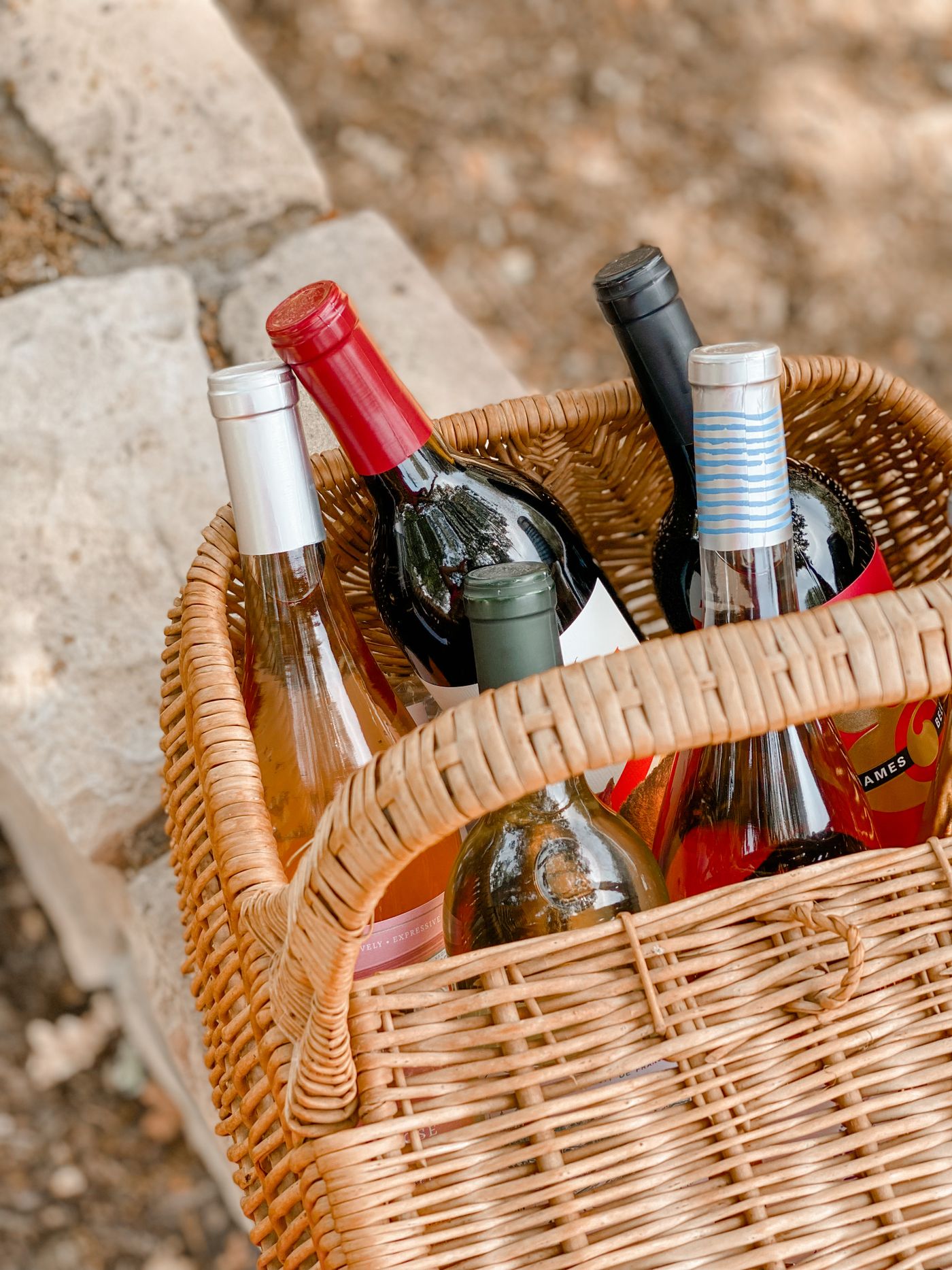 A hand-assembled wine gift basket with a bottle of red wine, wedges of cheese, crackers, and a ribbon