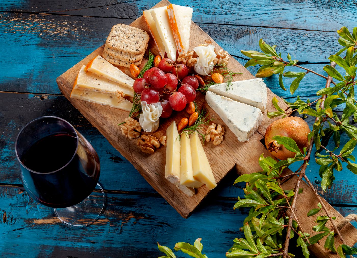 A glass of red wine beside a cheese board with grapes, crackers, and nuts for a wine and cheese gift