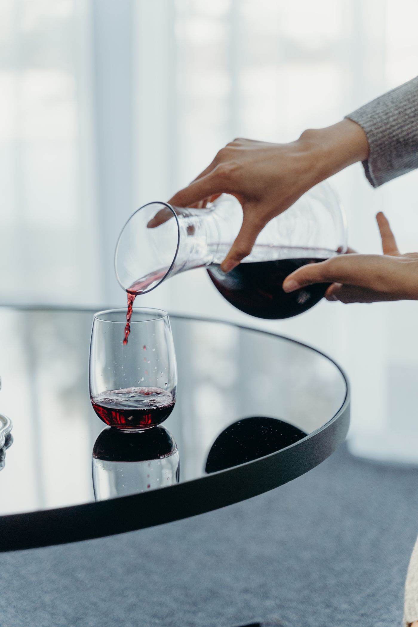 A wine aerator pouring red wine into a glass beside a decanter and a corkscrew arranged as affordable wine gifts