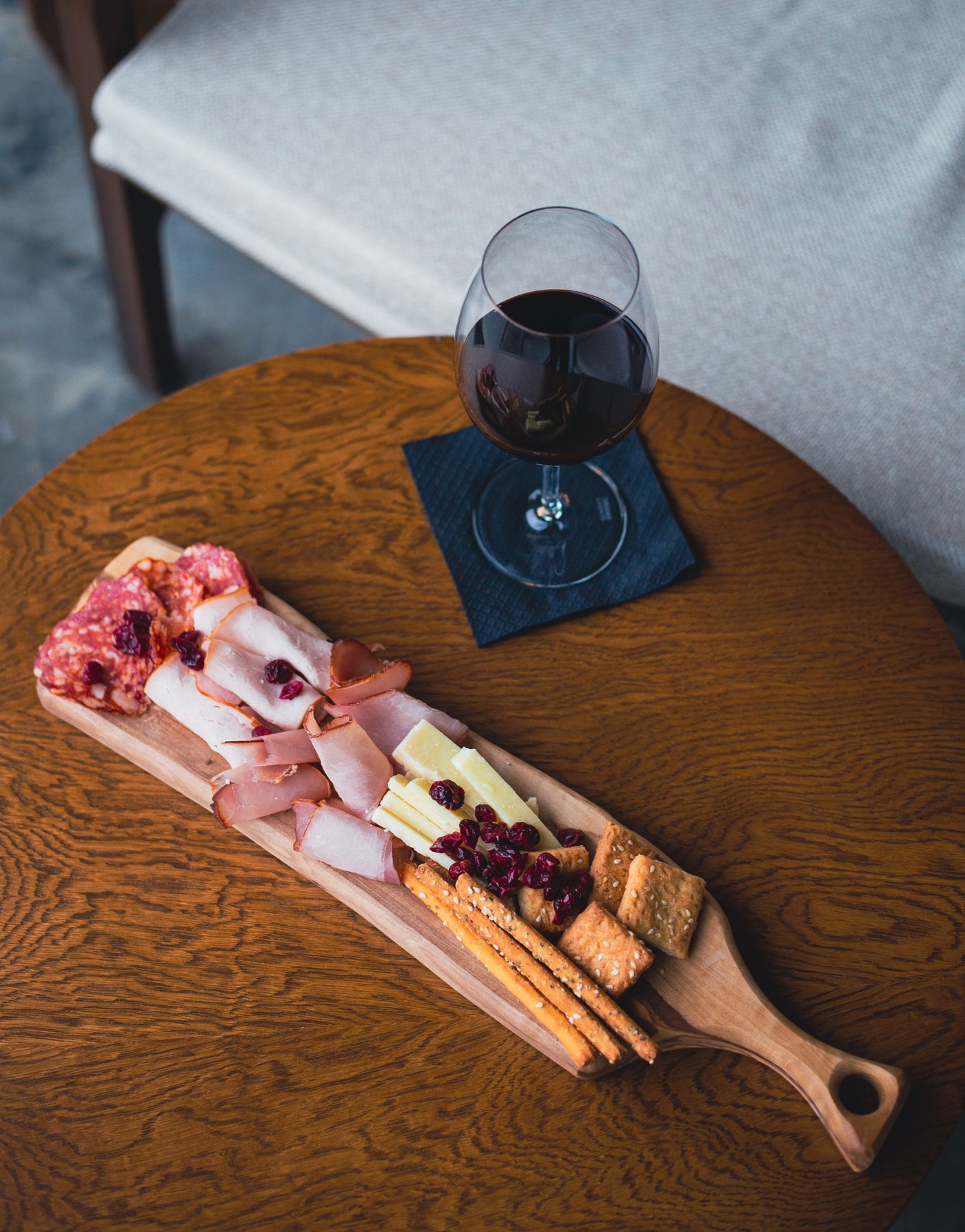 Hand pouring red wine into a glass next to a charcuterie board of cheese and cured meats showing a classic pairing